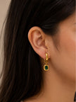 Gold-plated emerald green drop hoop earring worn on a womans ear with dark hair in the background