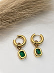 Pair of gold-plated emerald green cushion drop hoop earrings displayed on a white surface with dried pampas grass