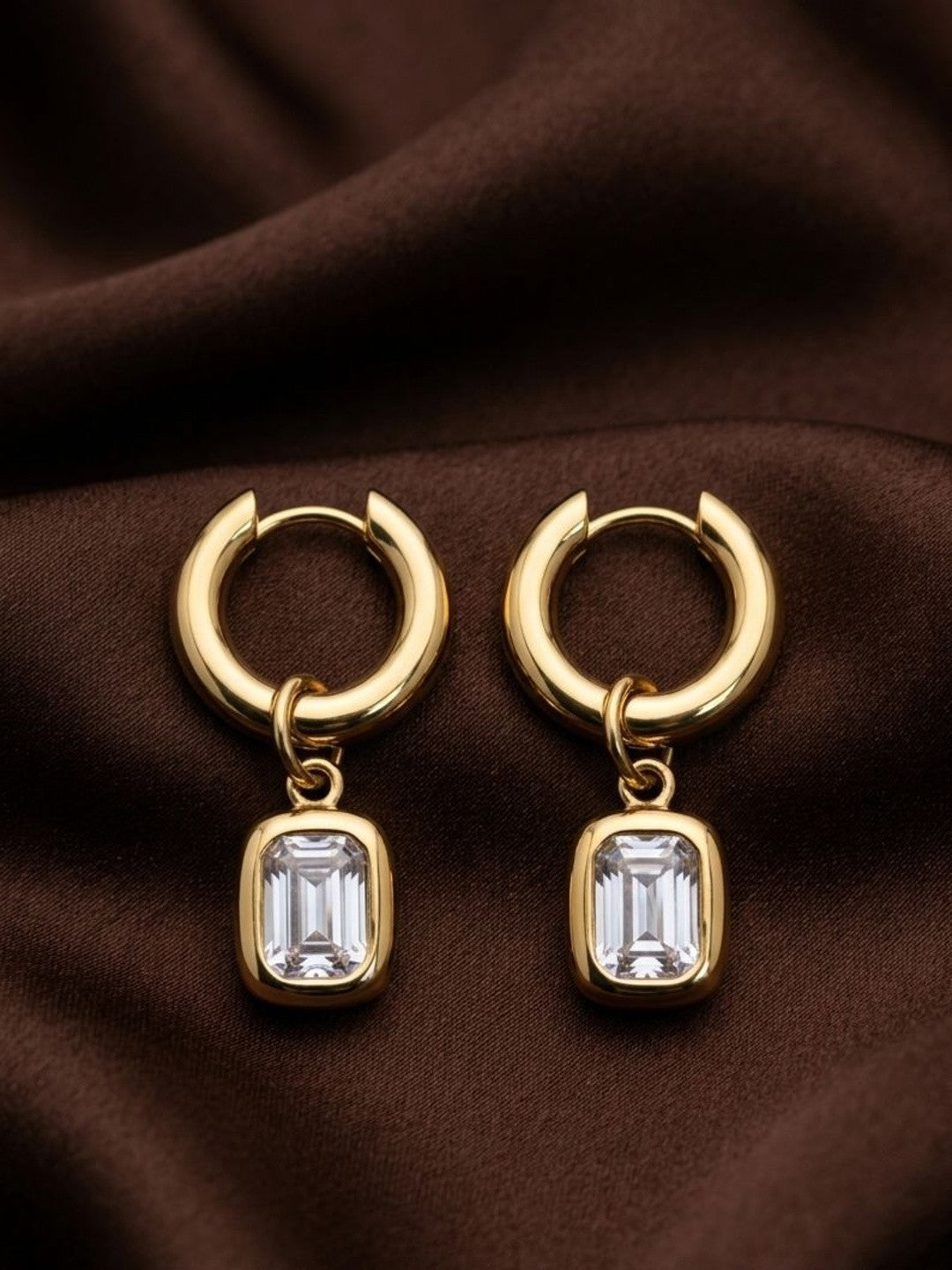 Pair of gold-plated chunky hoop earrings with emerald-cut crystal bezel charms on brown silk fabric