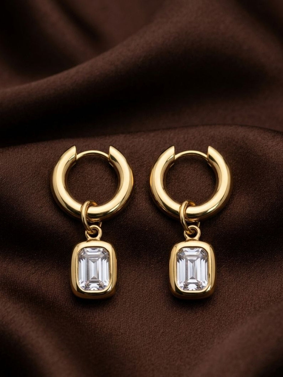Pair of gold-plated chunky hoop earrings with emerald-cut crystal bezel charms on brown silk fabric