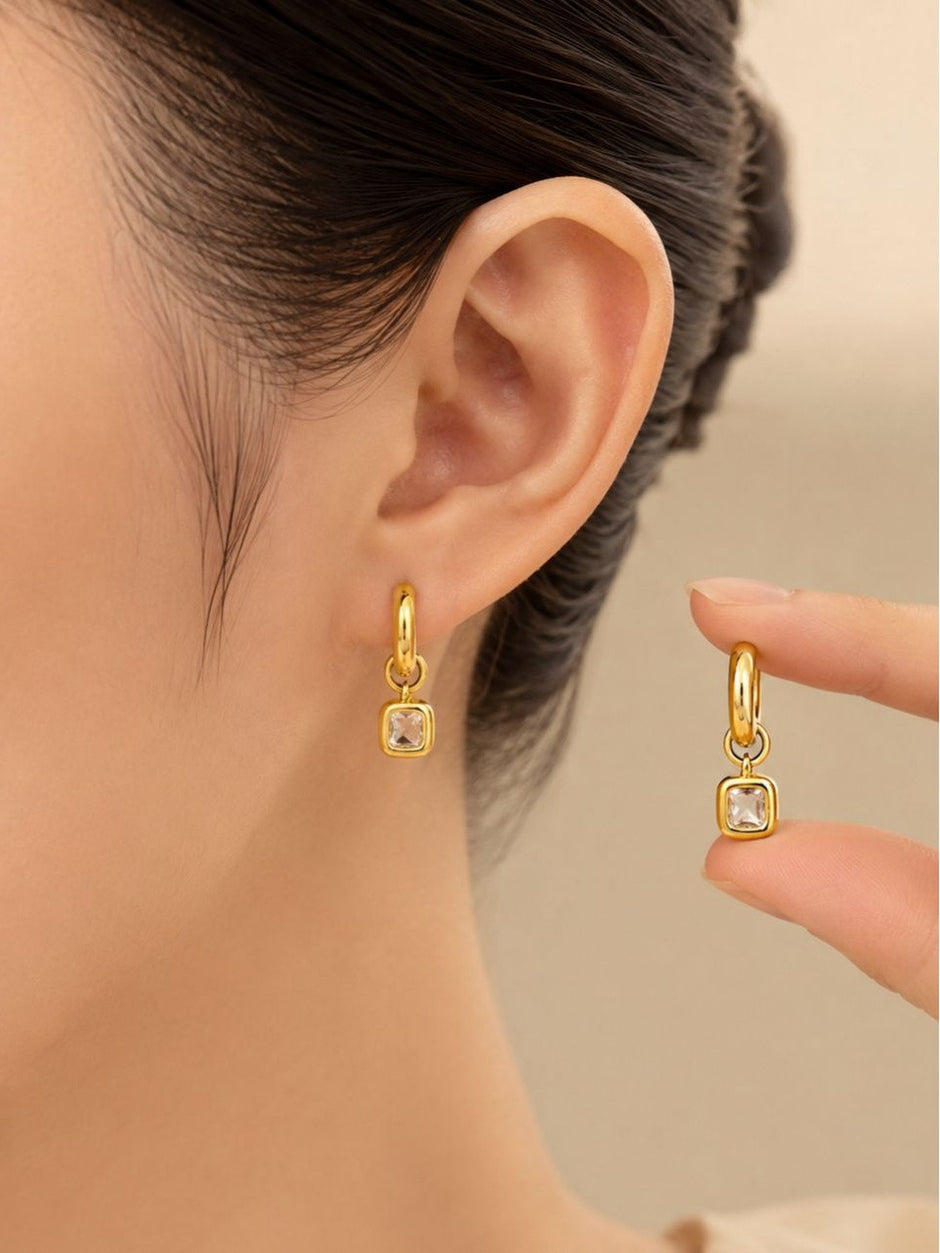 Woman wearing gold hoop crystal charm earring with second earring held between fingers showing scale