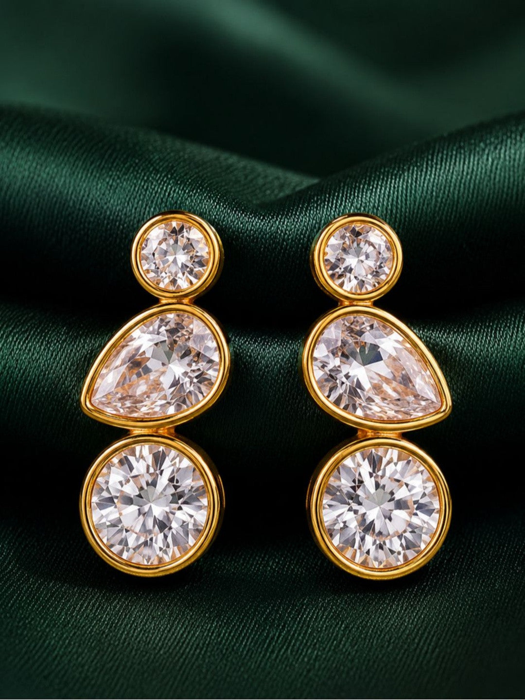 Pair of gold-plated bezel drop earrings with round pear and round crystal stones on green satin