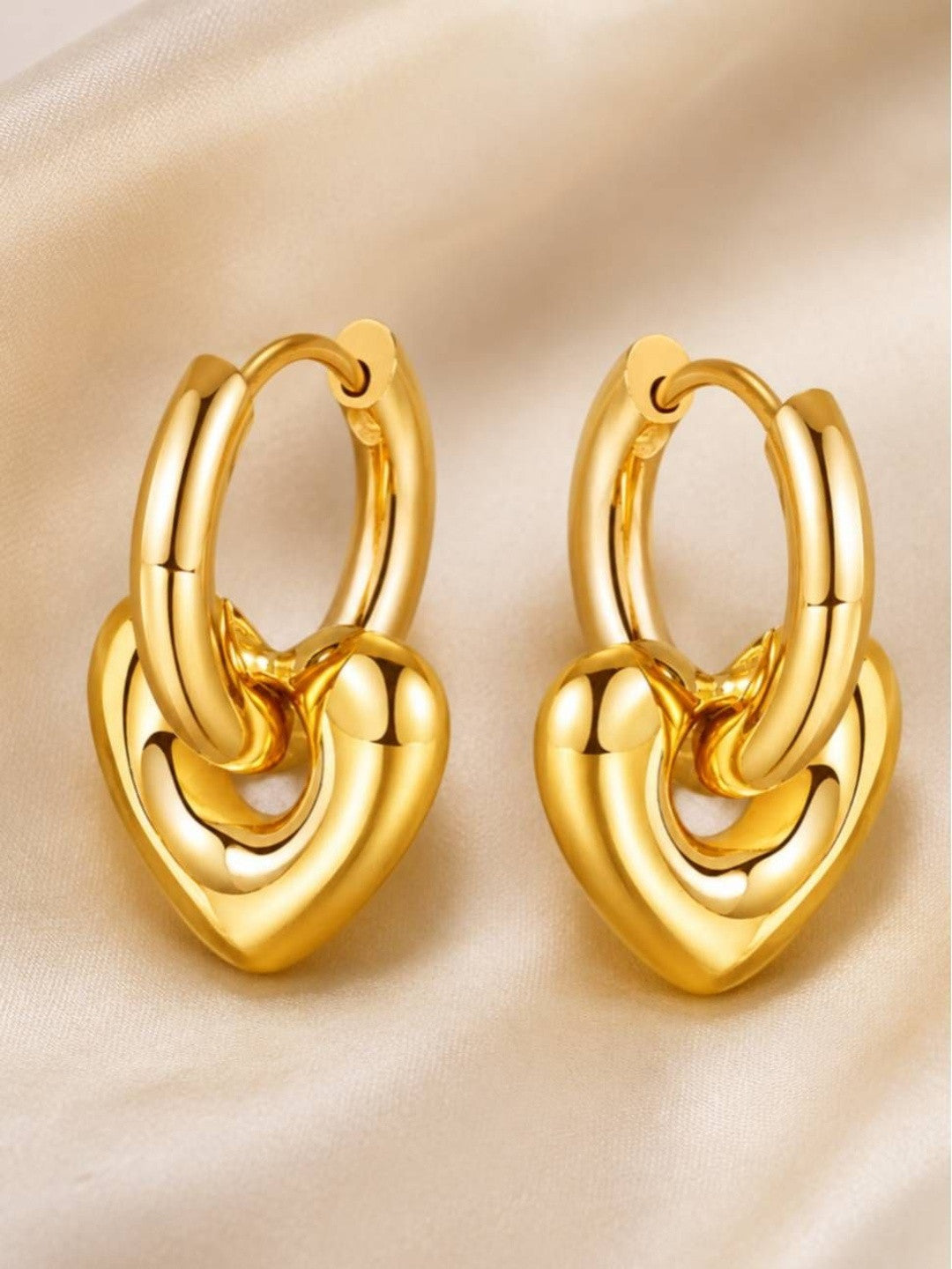 Close-up of chunky gold-plated puffy heart pendant hoops on cream satin background