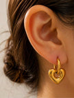 Gold heart drop hoop earring worn on a woman's ear showing size and fit
