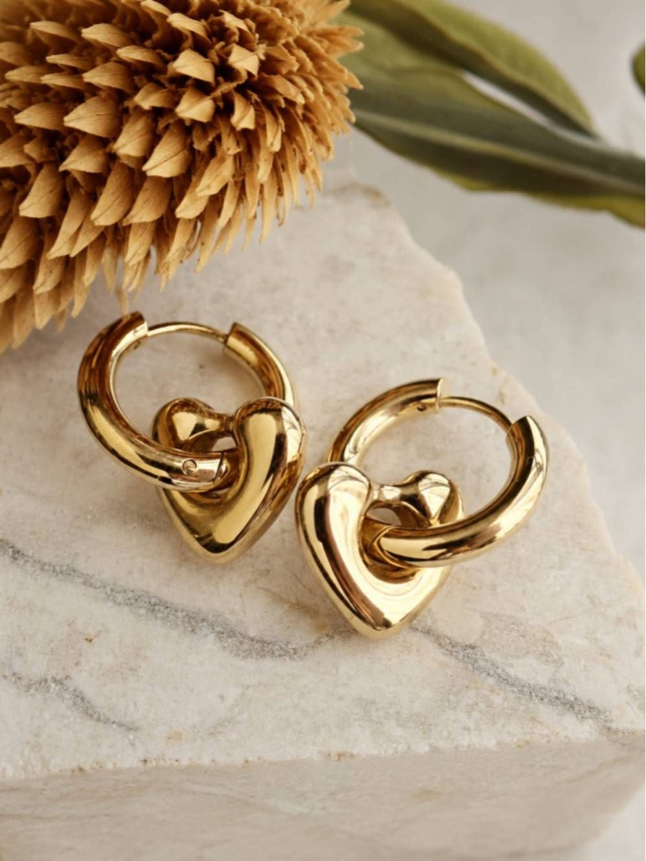 Gold-plated heart hoop earrings resting on a marble surface with dried flower styling
