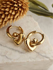 Gold-plated heart hoop earrings resting on a marble surface with dried flower styling