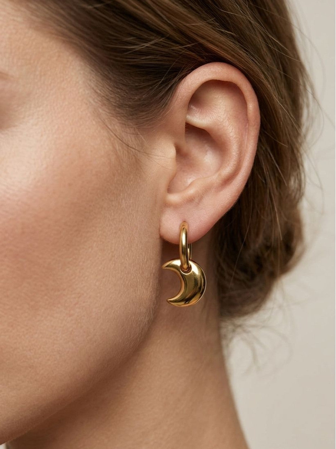Gold crescent moon hoop earring worn on a woman's ear showing scale and fit