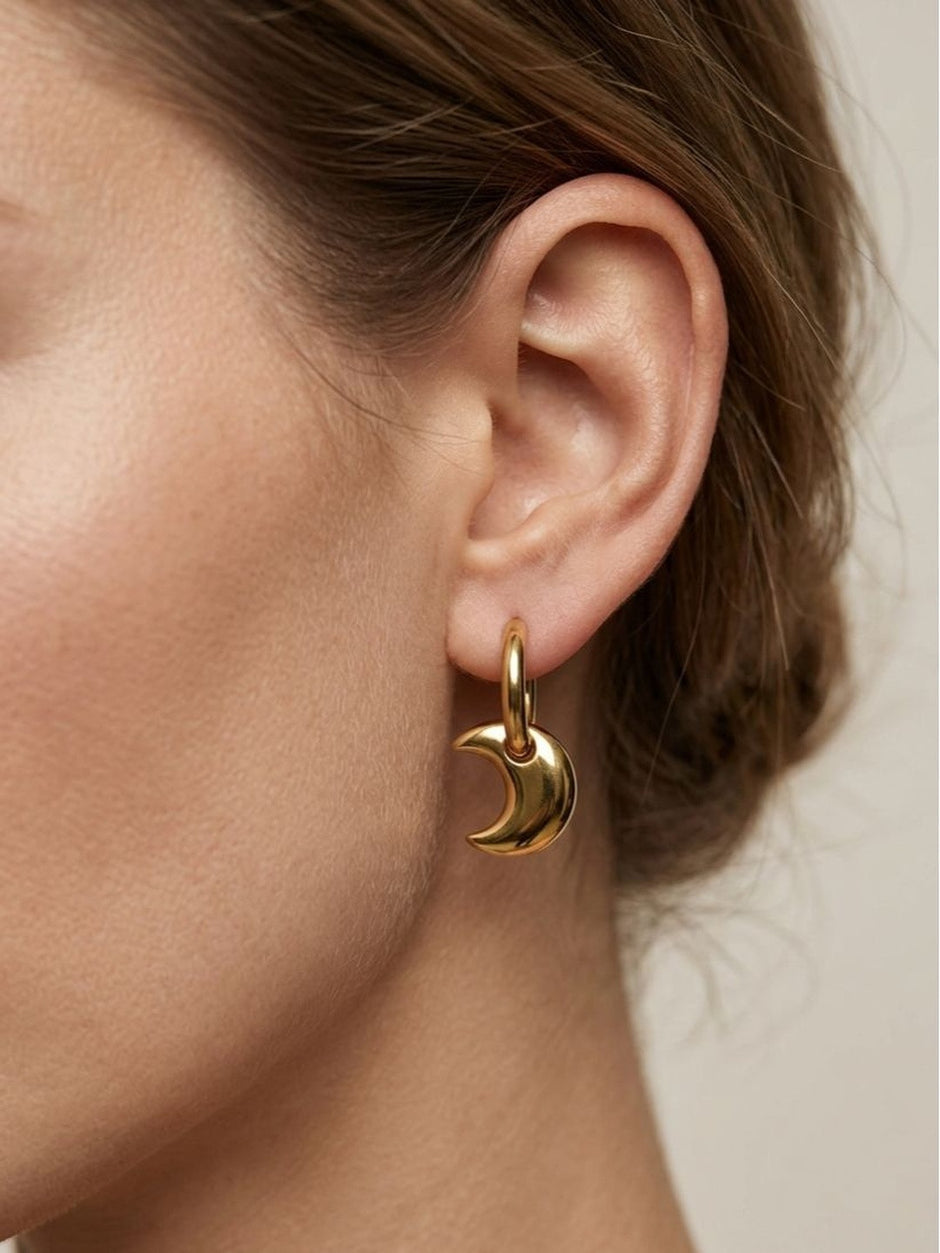 Gold crescent moon hoop earring worn on a woman's ear showing scale and fit