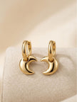 Two gold crescent moon charm hoops placed facing each other on a linen surface