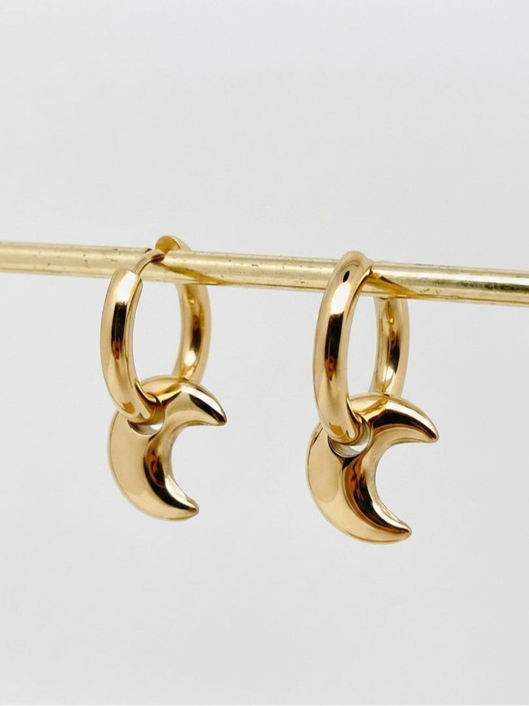 Gold crescent moon hoop earrings hanging from a brass rod against a white background