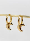 Gold crescent moon hoop earrings hanging from a brass rod against a white background
