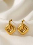 Pair of gold-plated geometric hoop drop earrings with hollow square pendants laid flat on white satin fabric