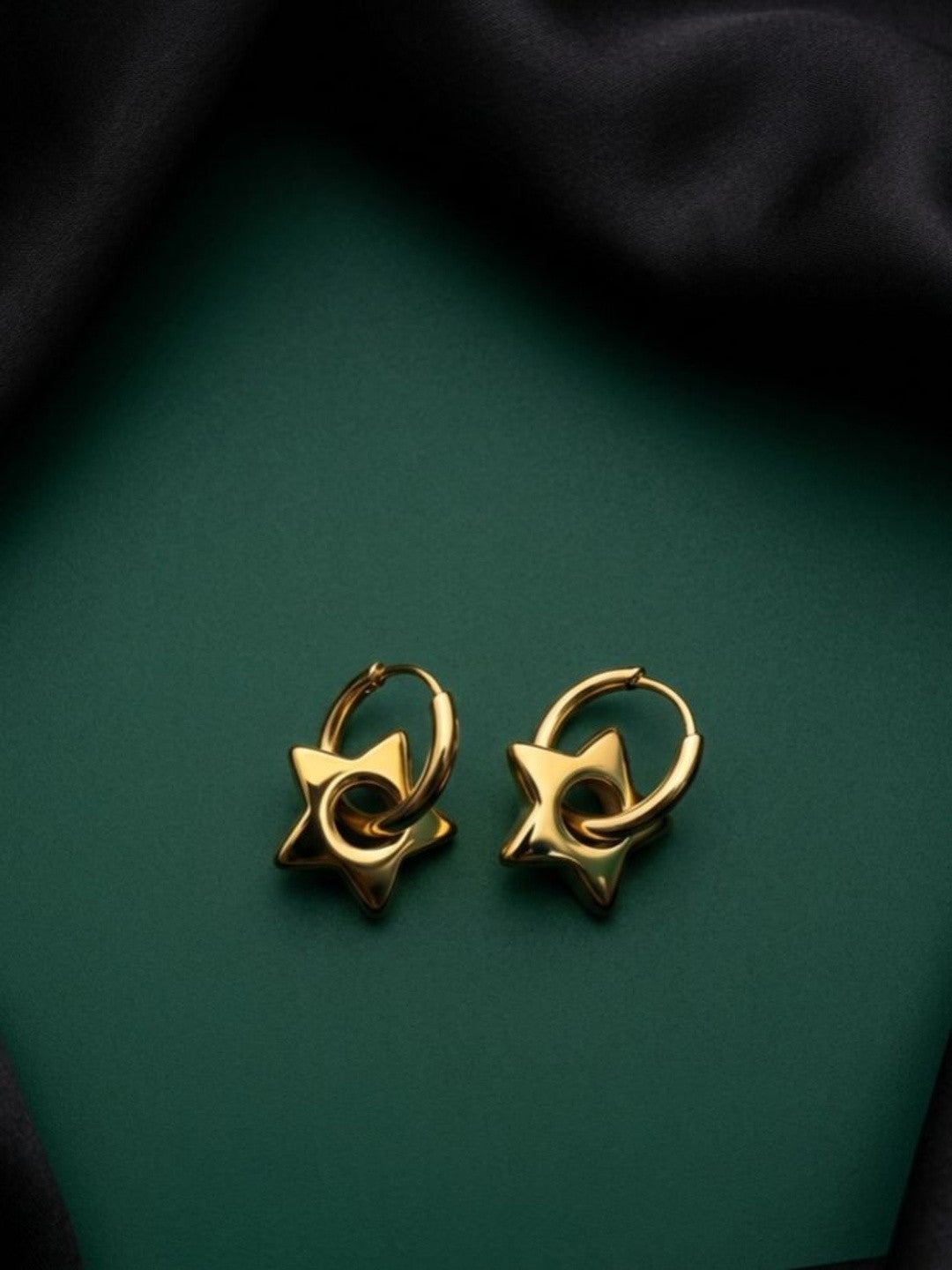 Pair of gold-plated star charm hoop earrings displayed flat on dark green surface