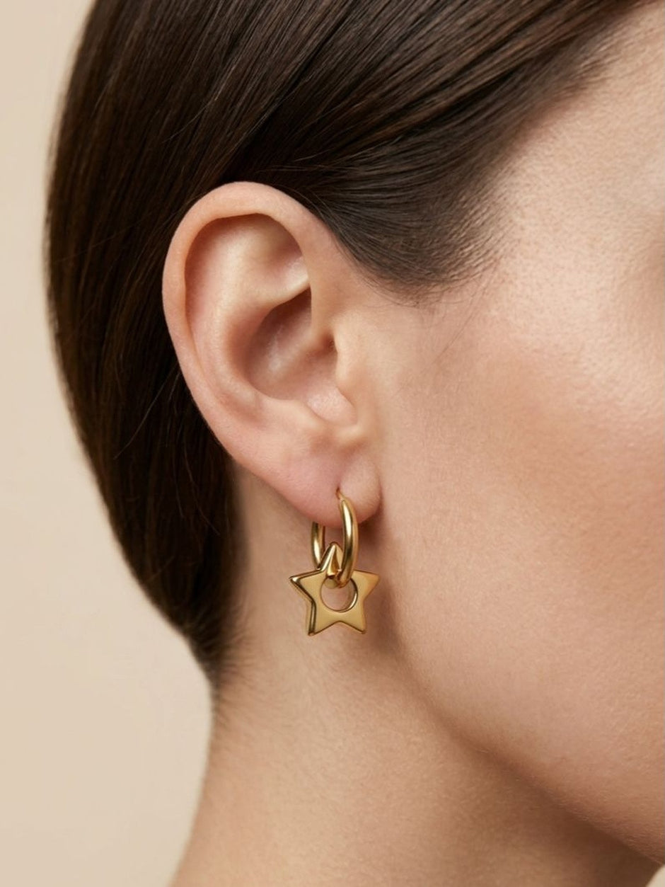 Close-up of gold star charm hoop earring worn on model's ear, side profile view