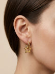 Close-up of gold star charm hoop earring worn on model's ear, side profile view
