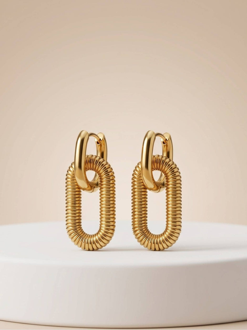 Pair of gold-plated ribbed oval link drop earrings standing upright on a white display pedestal