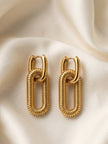 Two gold-plated ribbed oval link drop earrings laid flat on ivory silk fabric