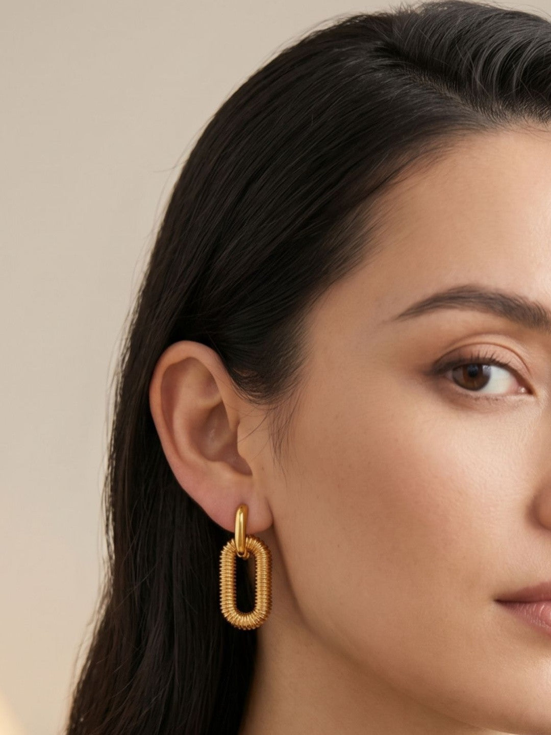 Close-up of a woman wearing one gold-plated ribbed oval link drop earring on her left ear