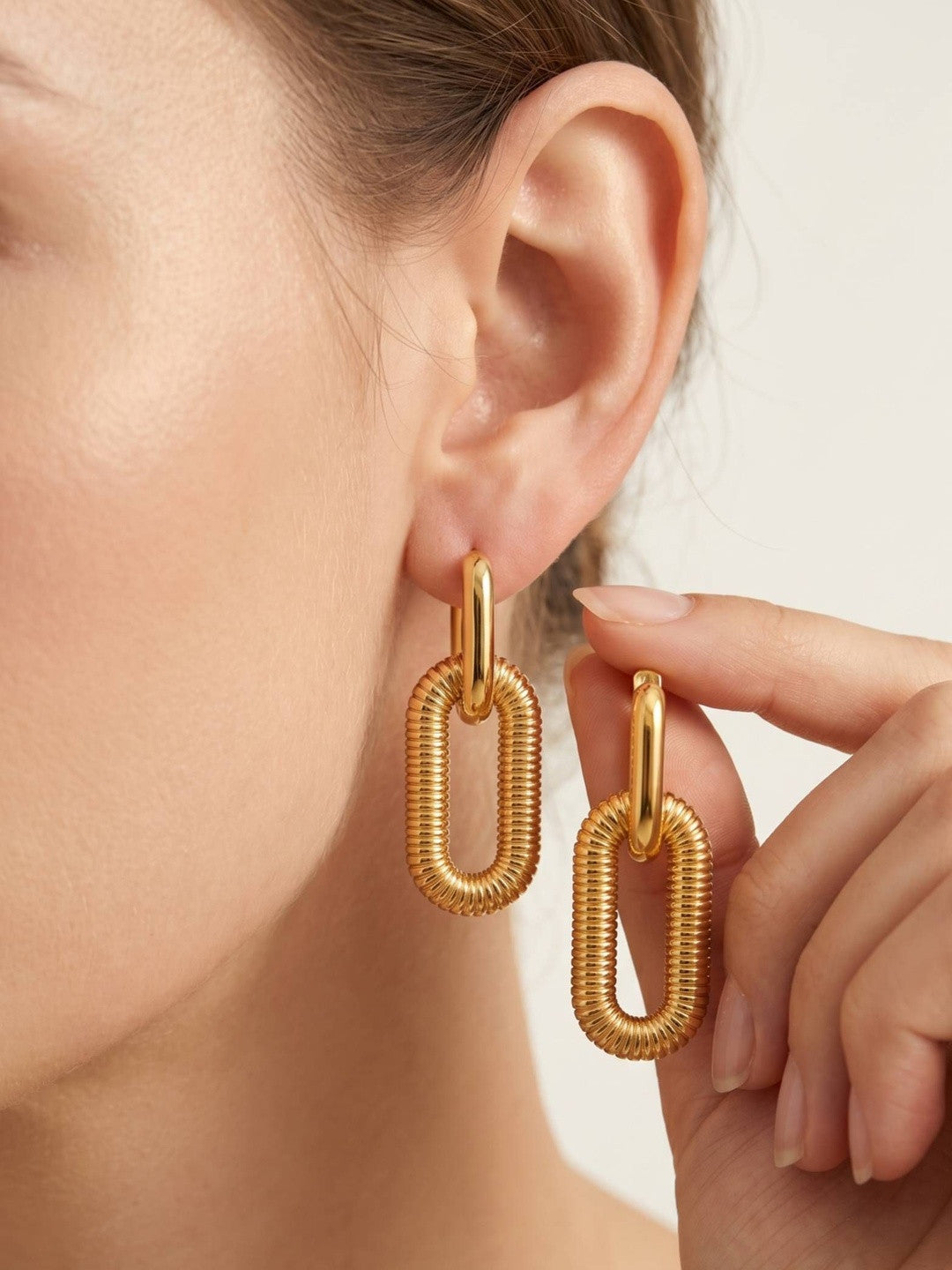 Woman wearing gold-plated ribbed link drop earring while holding the second earring between her fingers