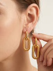Woman wearing gold-plated ribbed link drop earring while holding the second earring between her fingers