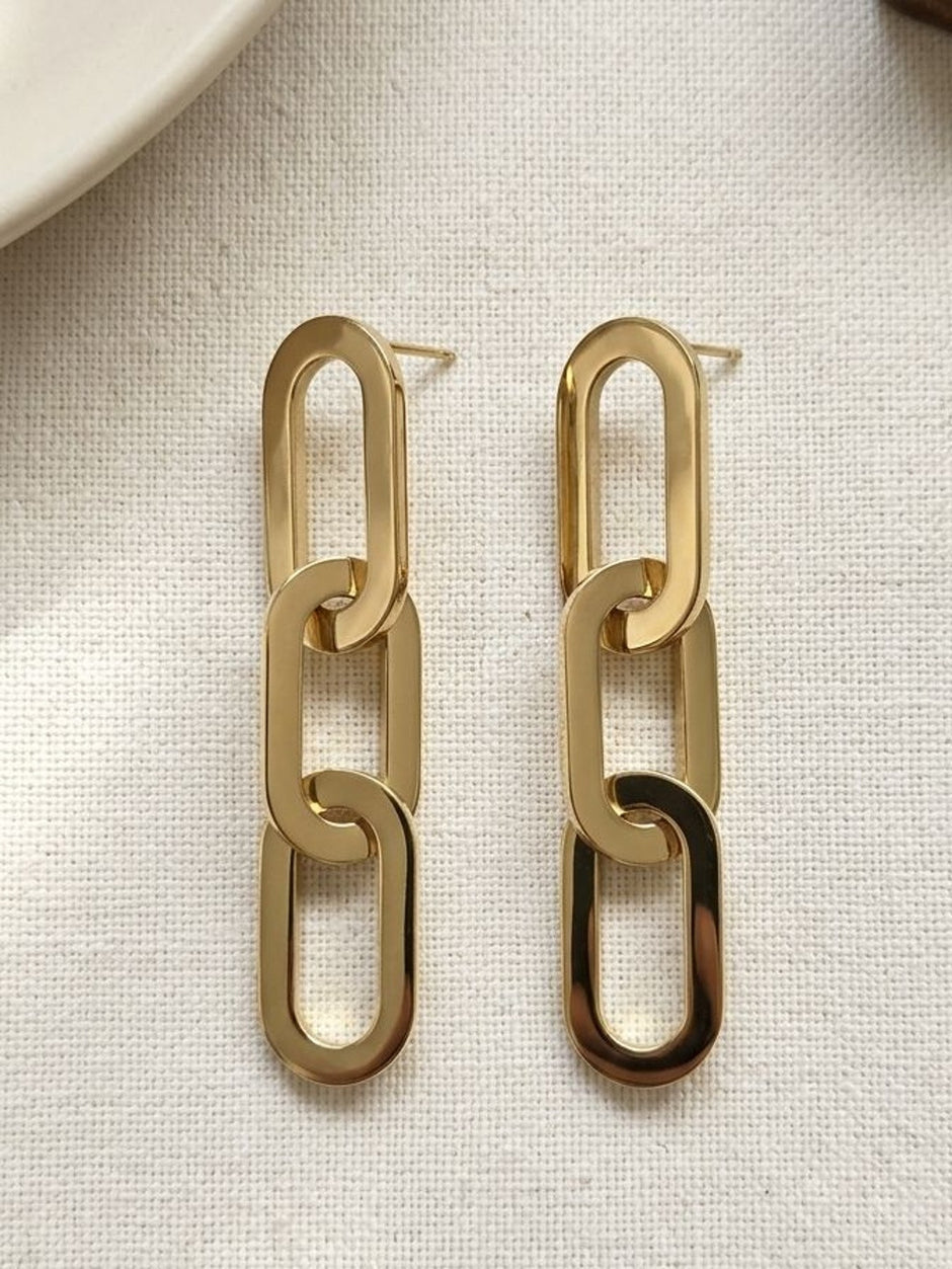Pair of gold-toned chain link drop earrings laid flat on a cream linen background showing stud posts