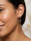 Woman wearing gold oval chain link drop earring, smiling, hair pulled back, close-up side view