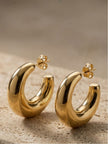 Pair of chunky gold-plated oval half hoop earrings with push-back posts resting on a textured stone surface