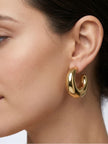 Close-up side profile of a woman wearing a single chunky gold-plated oval half hoop earring on her left ear
