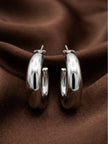 Pair of chunky silver-finish hoop earrings laid flat on rich brown fabric