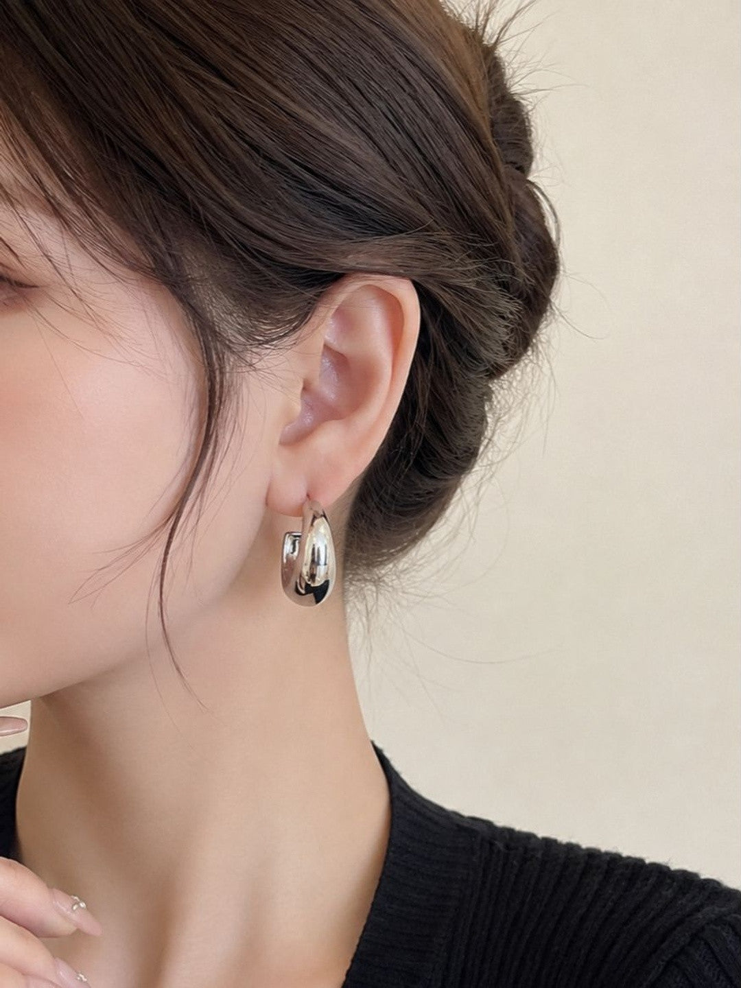 Close-up of chunky silver hoop earring worn on a woman's ear with dark upswept hair