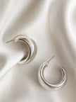 Pair of chunky silver tubular hoop earrings placed on draped white satin fabric