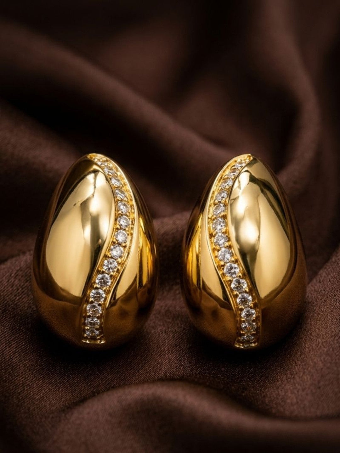 Pair of gold-plated teardrop stud earrings with cubic zirconia diagonal line on draped brown fabric