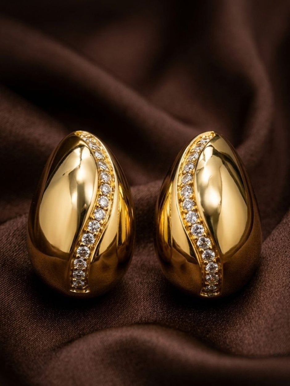 Pair of gold-plated teardrop stud earrings with cubic zirconia diagonal line on draped brown fabric