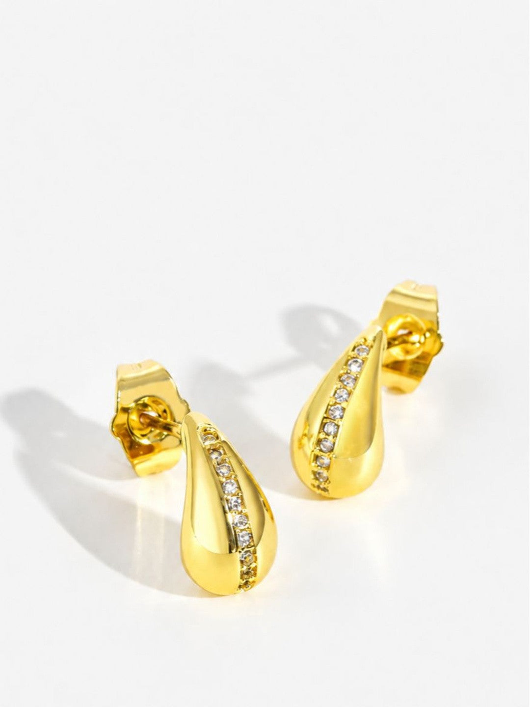 Side angle of gold-plated teardrop stud earrings showing depth of dome and zirconia channel setting on white surface