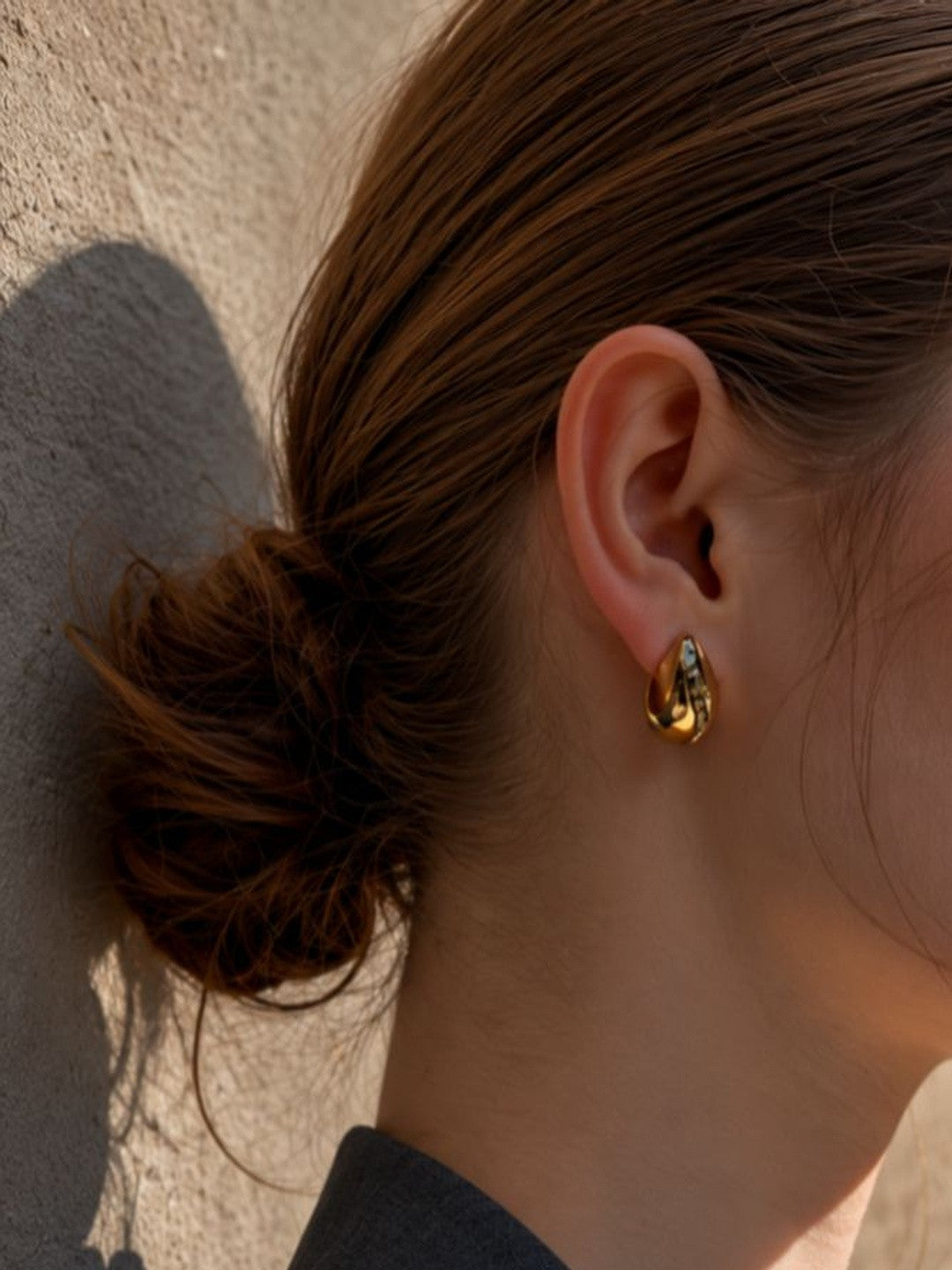Gold-plated teardrop stud earring worn on a woman's earlobe with hair pulled back in a bun