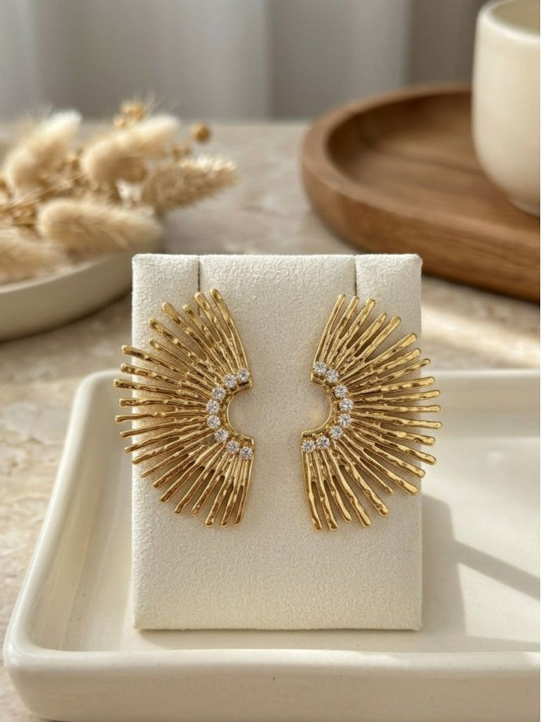 Pair of gold-toned sunburst fan stud earrings with zirconia stones displayed on a white jewellery card