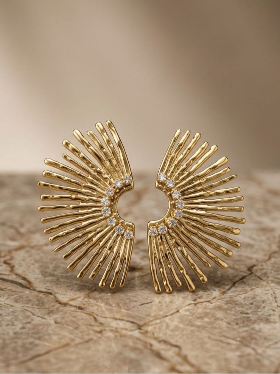 Close-up front view of gold sunburst earrings with hammered spoke texture and crescent zirconia arc on stone surface