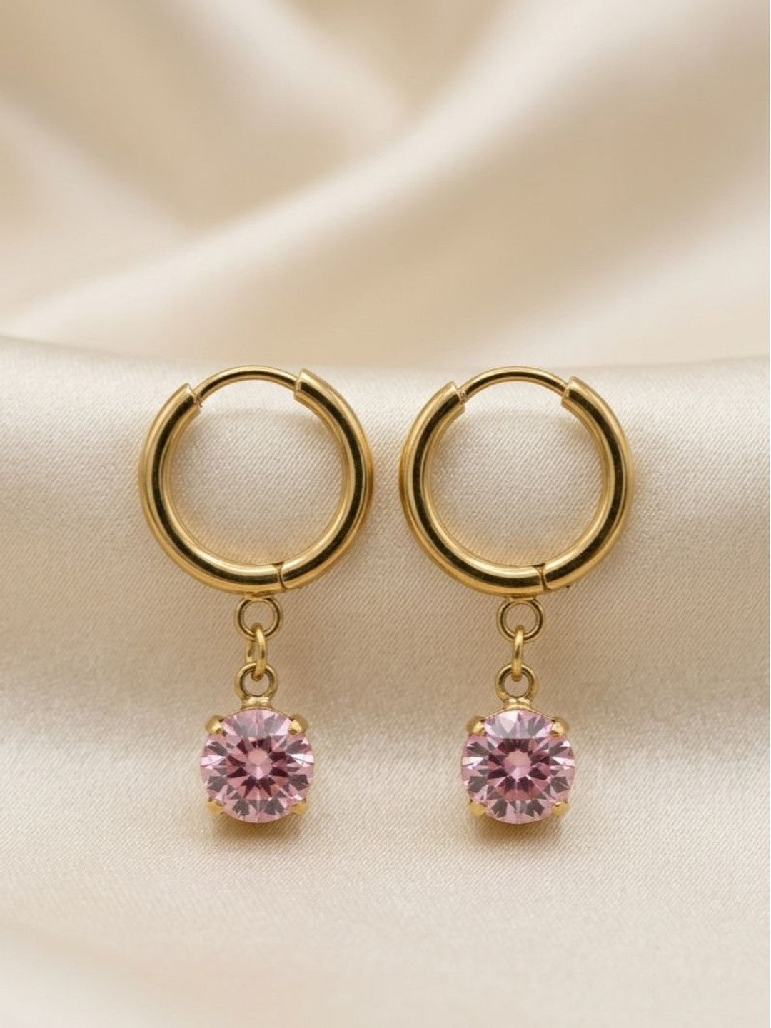Pair of gold-plated huggie hoop earrings with pink round stone charm on white satin