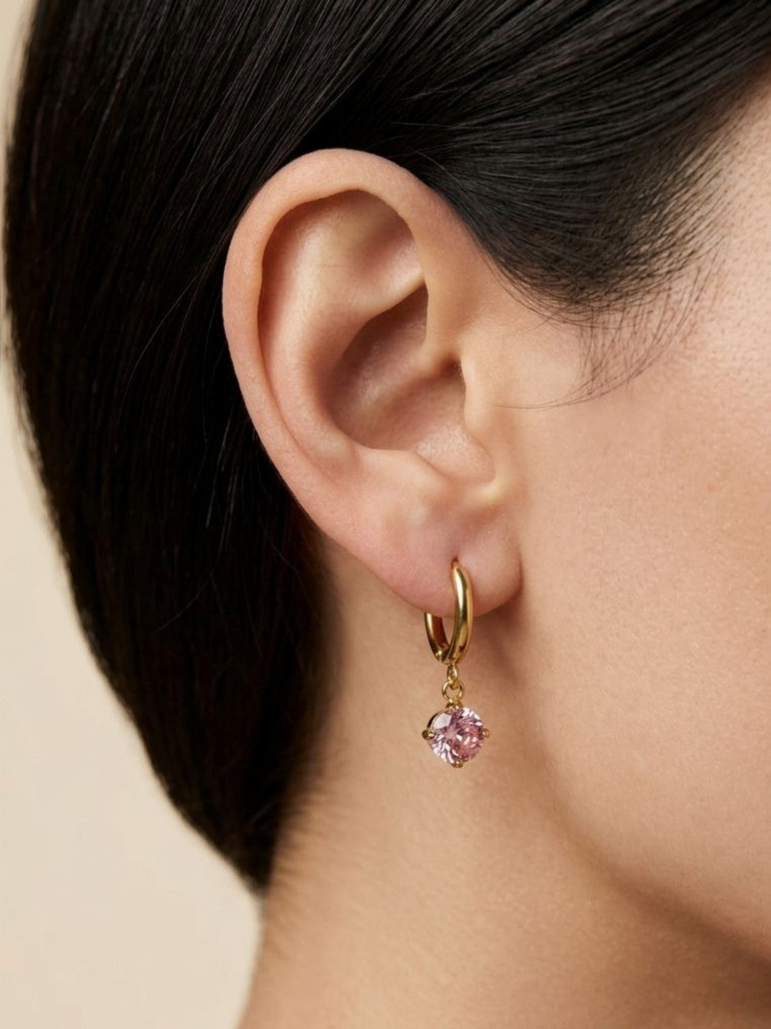 Gold hoop earring with pink stone charm worn on a woman's ear, side profile view