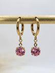 Gold-plated hoop earrings with pink stone charms hanging from a gold display bar