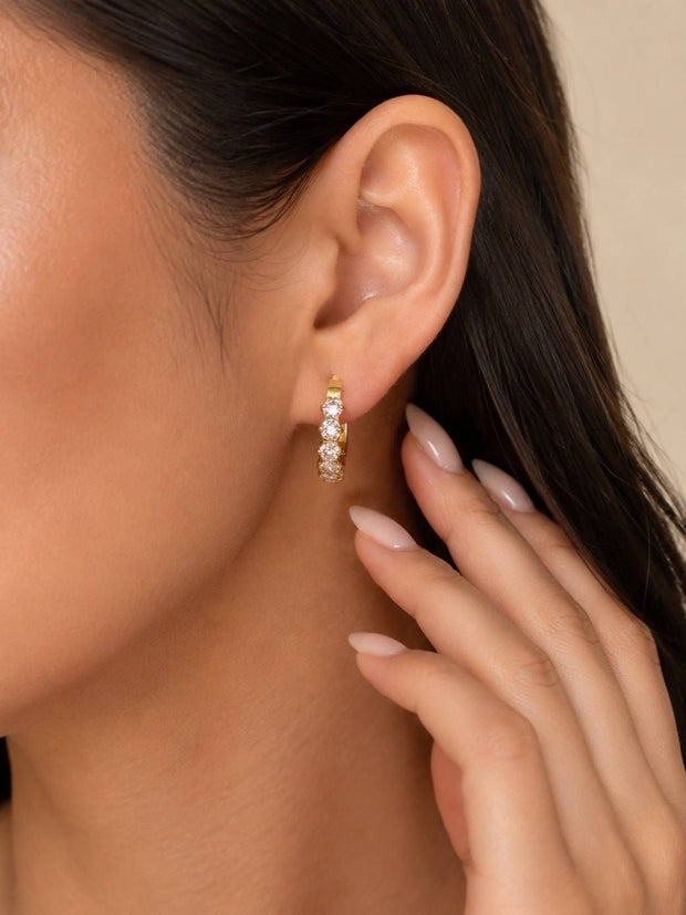 Close-up of gold CZ huggie hoop earring worn on a model's ear, hand resting near cheek