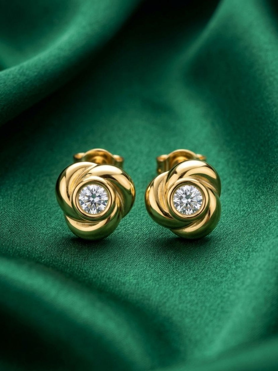 Pair of gold-plated swirl knot stud earrings with round crystal centres on green satin fabric