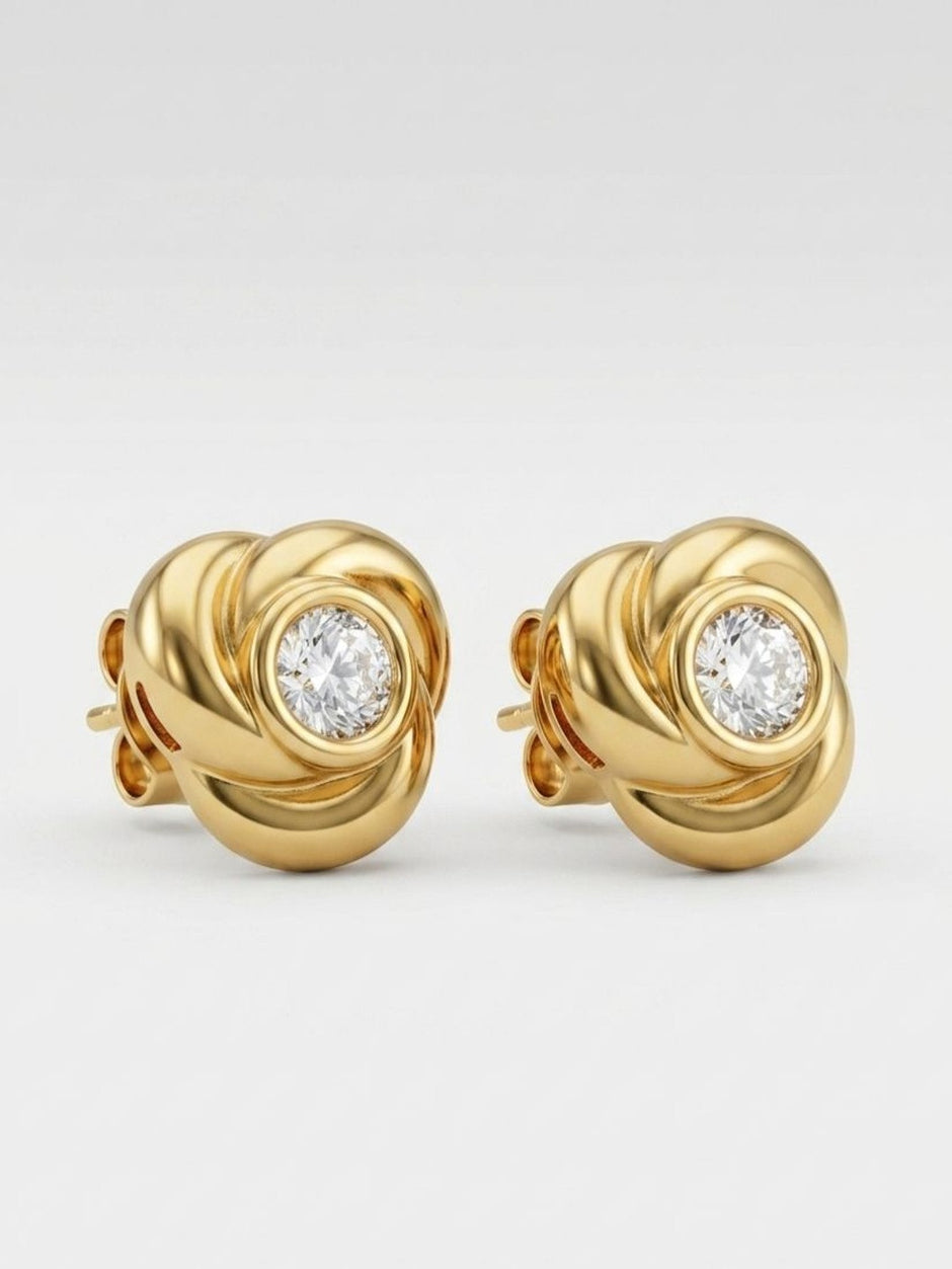 Close-up of gold-plated knot stud earrings showing spiral detail and bezel-set crystal on white background