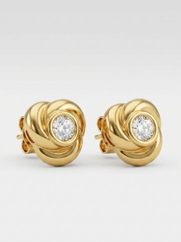 Close-up of gold-plated knot stud earrings showing spiral detail and bezel-set crystal on white background