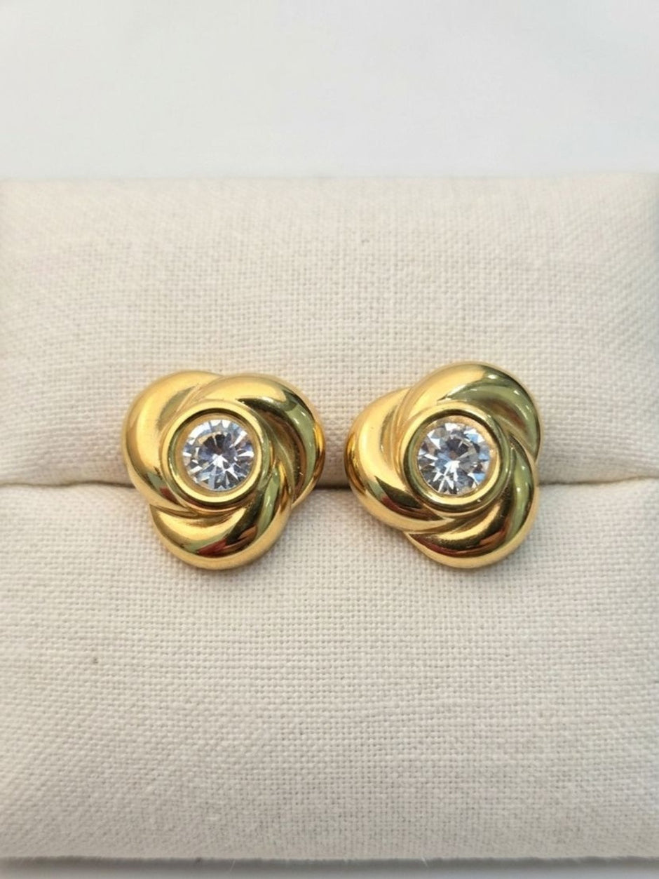 Pair of gold-plated swirl knot studs with crystal centres displayed on cream jewellery cushion