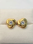 Pair of gold-plated swirl knot studs with crystal centres displayed on cream jewellery cushion