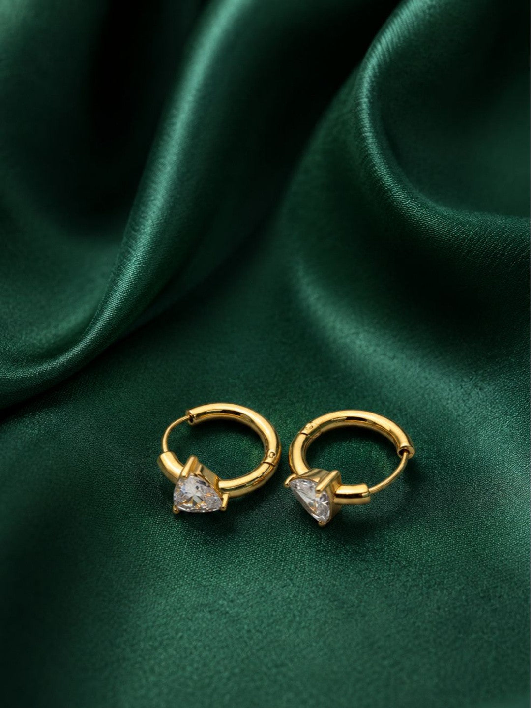 Pair of gold-plated huggie hoop earrings with heart-shaped CZ stones on green satin fabric