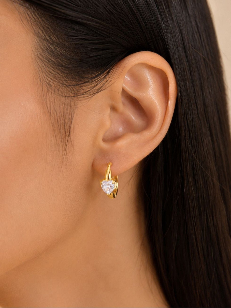 Close side view of gold heart CZ huggie hoop earring worn on model's ear
