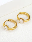 Two gold-plated heart CZ huggie hoop earrings laid flat on white textured surface