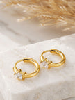 Pair of gold-plated huggie hoop earrings with star-cut cubic zirconia, displayed on a white marble surface